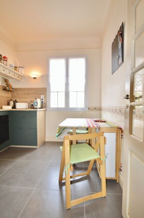 A compact kitchen with a dining table and chairs, a window, and a door. - Vrbo Property (Biarritz)