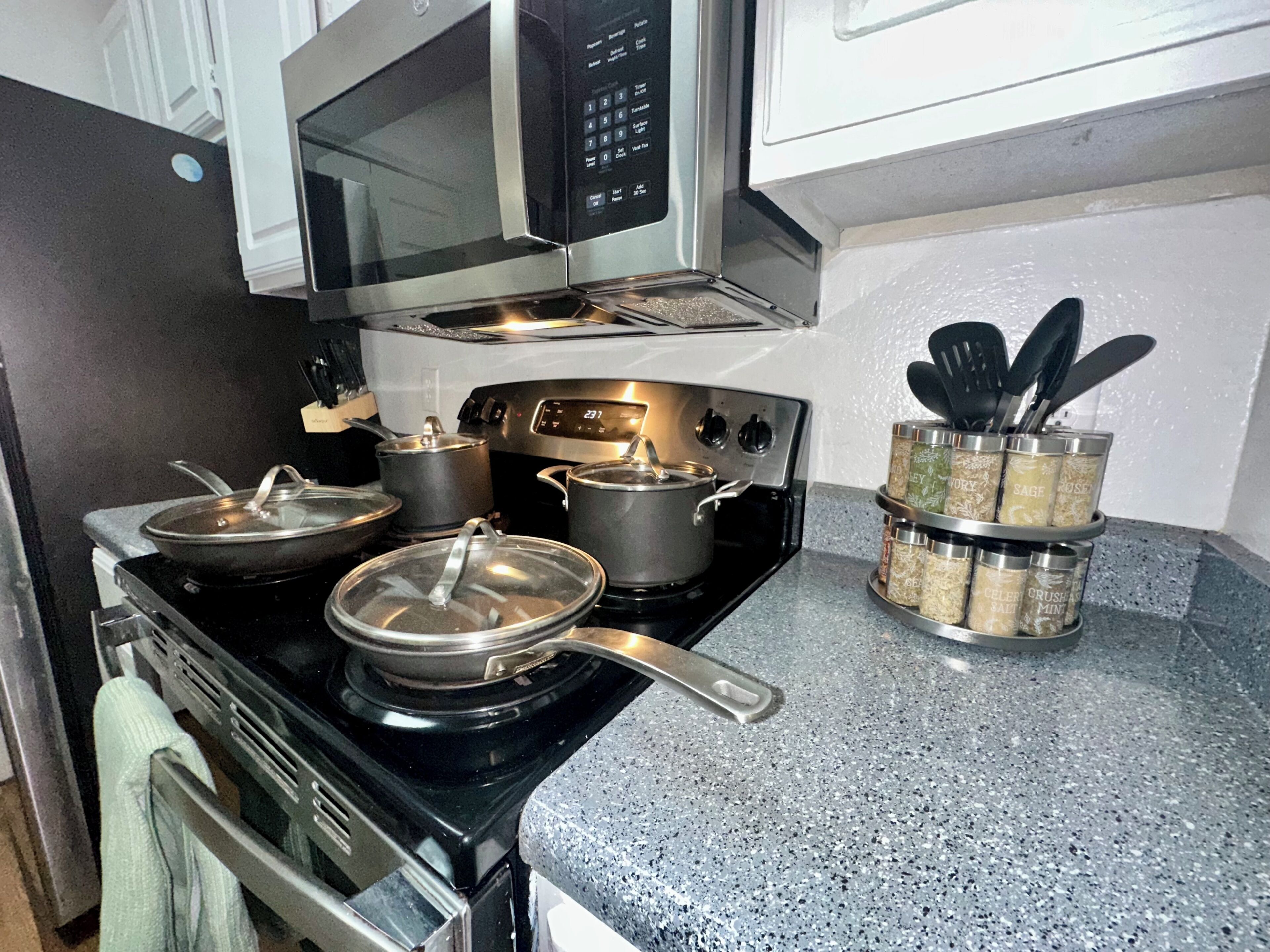 A kitchen with a stove, pots, a microwave, and spice jars on the counter.