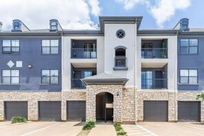 A multi-story residential building with stone facade, multiple balconies, and garage doors. - Las Colinas Retreat Near Toyota Music Factory, DFW & Convention Ctr (Irving)