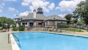 Une piscine dotée d’une rambarde métallique, de chaises longues et d’un bâtiment en pierre avec une tour en arrière-plan.