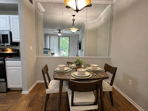 A dining area with a table set for four, a kitchen in the background, and a large mirror reflecting the room. - Las Colinas Retreat Near Toyota Music Factory, DFW & Convention Ctr (Irving)