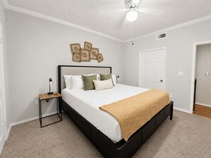 Un dormitorio con cama, mesita de noche, decoración en la pared y ventilador de techo.