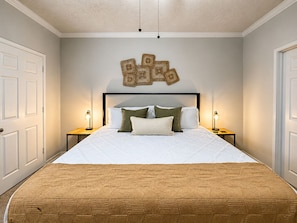 A bedroom with a bed, two bedside tables, a wall-mounted light fixture, and a door.