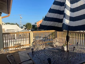 Eine Terrasse mit einem Metalltisch, Stühlen, einem gestreiften Sonnenschirm und Blick auf die Straße.
