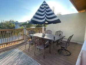En terrass med ett bord och stolar, ett randigt parasoll och utsikt över kvarteret.