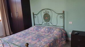 A bed with a floral bedspread, a metal headboard with a decorative plate, a dark wooden wardrobe, and a small bedside table with a drawer. - Relax nel Verde 1 - One Bedroom Apartment, Sleeps 2 (Calafuria)