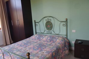A bed with a floral bedspread, a metal headboard with a decorative plate, a dark wooden wardrobe, and a small bedside table with a drawer. - Relax nel Verde 1 - One Bedroom Apartment, Sleeps 2 (Calafuria)