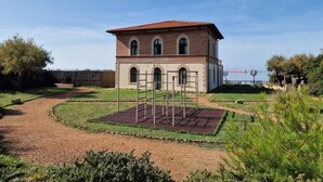 A two-story building with a red-tiled roof and arched windows, surrounded by a landscaped garden with a gravel path. - Relax nel Verde 1 - One Bedroom Apartment, Sleeps 2 (Calafuria)