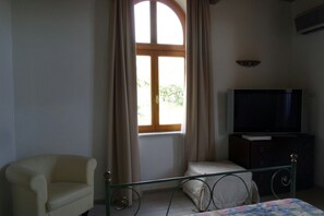 Ein Schlafzimmer mit Bett, Stuhl, Fernseher und einem Fenster mit Vorhängen.