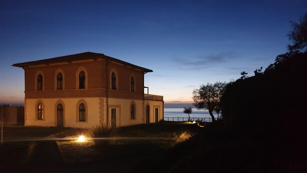 A two-story building with arched windows and a balcony, located near a body of water. - Relax nel Verde 1 - One Bedroom Apartment, Sleeps 2 (Calafuria)