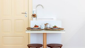 Una pequeña cocina con encimera blanca, un lavamanos y dos taburetes.