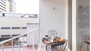 En balkong med ett bord dukat för frukost, en stol och utsikt över en byggnad.