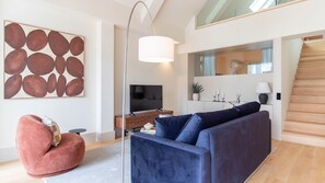 A modern living room with a blue sofa, a red chair, a flat-screen TV, and a large abstract painting. - Catarina 392 | Premium Duplex by LovelyStay (Porto)