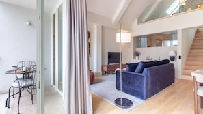 Ein modernes Wohnzimmer mit einer Couch, einem Esstisch mit Stühlen, einem Fernseher und einer Treppe.