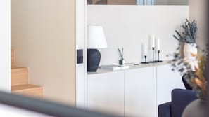 Ein modernes Interieur mit einer Holztreppe, einem weißen Empfangstresen, einer Lampe, Kerzen und einer Vase mit Grünpflanzen.