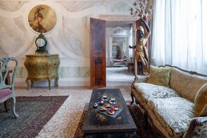 Una habitación con un sofá, una mesa de centro con pasteles, un reloj, una estatua y un cuadro en la pared.