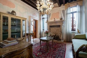 Una habitación con chimenea, candelabro, sofá verde y alfombra estampada.
