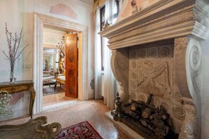 Un amplio pasillo con chimenea, muebles ornamentados y una puerta que da a otra habitación.