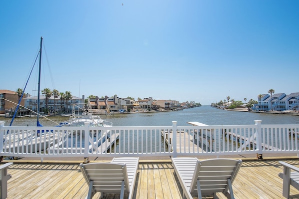 A wooden deck with white railings, overlooking a marina with boats and waterfront buildings. - Surf Studio (Corpus Christi)
