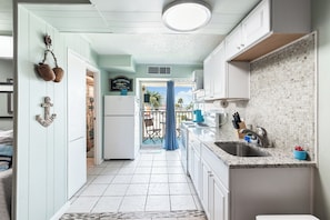 A kitchen with a tiled backsplash, a sink, and a countertop with kitchen utensils. - Surf Studio (Corpus Christi)
