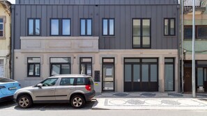 En modern byggnad i två våningar med en grå fasad, stora fönster och en bil parkerad framför.