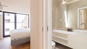 Un dormitorio moderno con una cama grande, un balcón y un baño con un espejo amplio y elementos blancos.