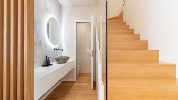Un bagno moderno con pavimento in legno, un ampio specchio ovale e un lavabo a incasso.