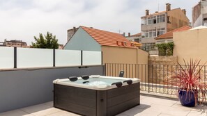 Una terraza con bañera de hidromasaje, una planta en maceta y vistas de edificios circundantes.