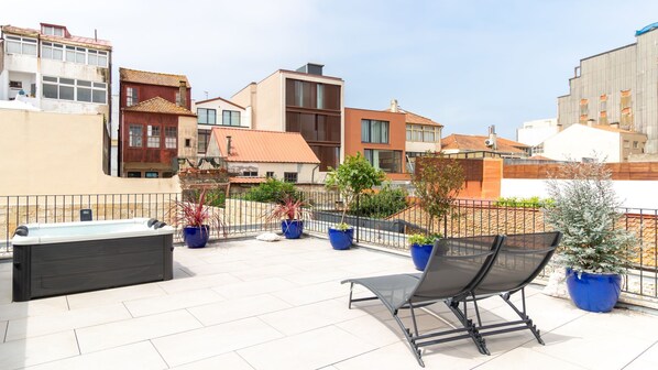 En tagterrasse med jacuzzi, siddeområde, plantekasser og udsigt til omkringliggende bygninger.
