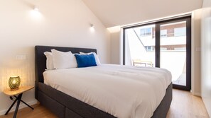 Et moderne soveværelse med en stor seng, et lille natbord og udsigt ud.