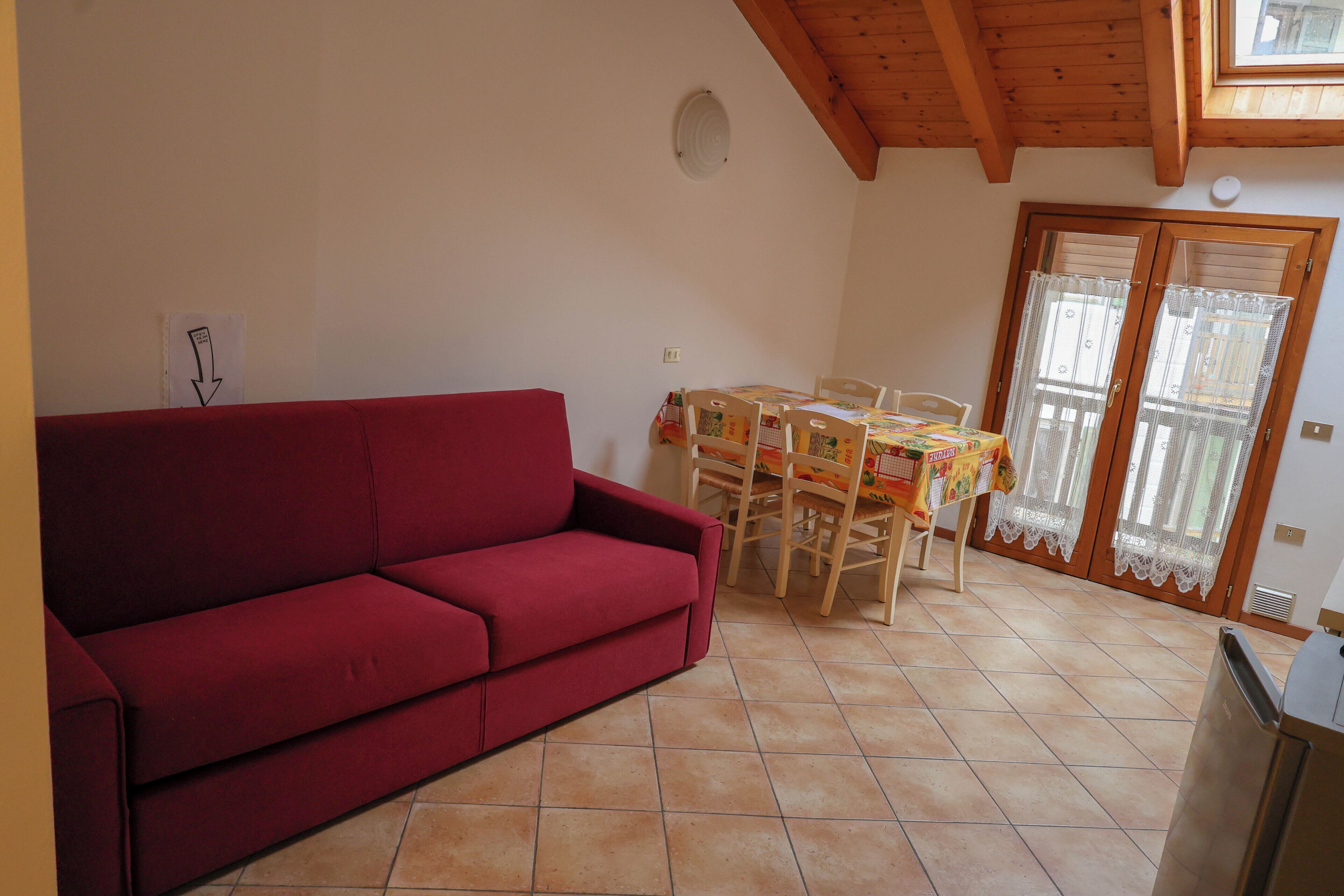 A red sofa, a dining table with chairs, a kitchen area, and a sliding glass door.