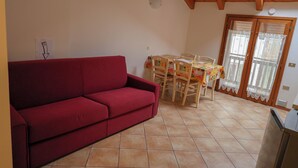 A red sofa, a dining table with chairs, a kitchen area, and a sliding glass door. - Apartment 6 Maso Anna (Mastellina)
