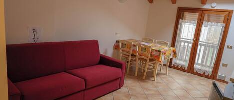 A red sofa, a dining table with chairs, a kitchen area, and a sliding glass door.