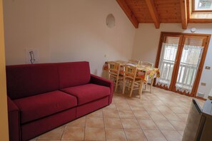 A red sofa, a dining table with chairs, a kitchen area, and a sliding glass door. - Vrbo Property (Mastellina)