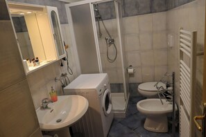 A bathroom with a sink, washing machine, toilet, and shower. - Vrbo Property (Mastellina)
