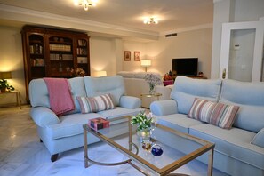 Ein Wohnzimmer mit einer Sofagarnitur, einem Couchtisch, einem Bücherregal und einem Fernseher.