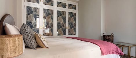A bedroom with a bed, a window with a view, a ceiling fan, and a bedside table.