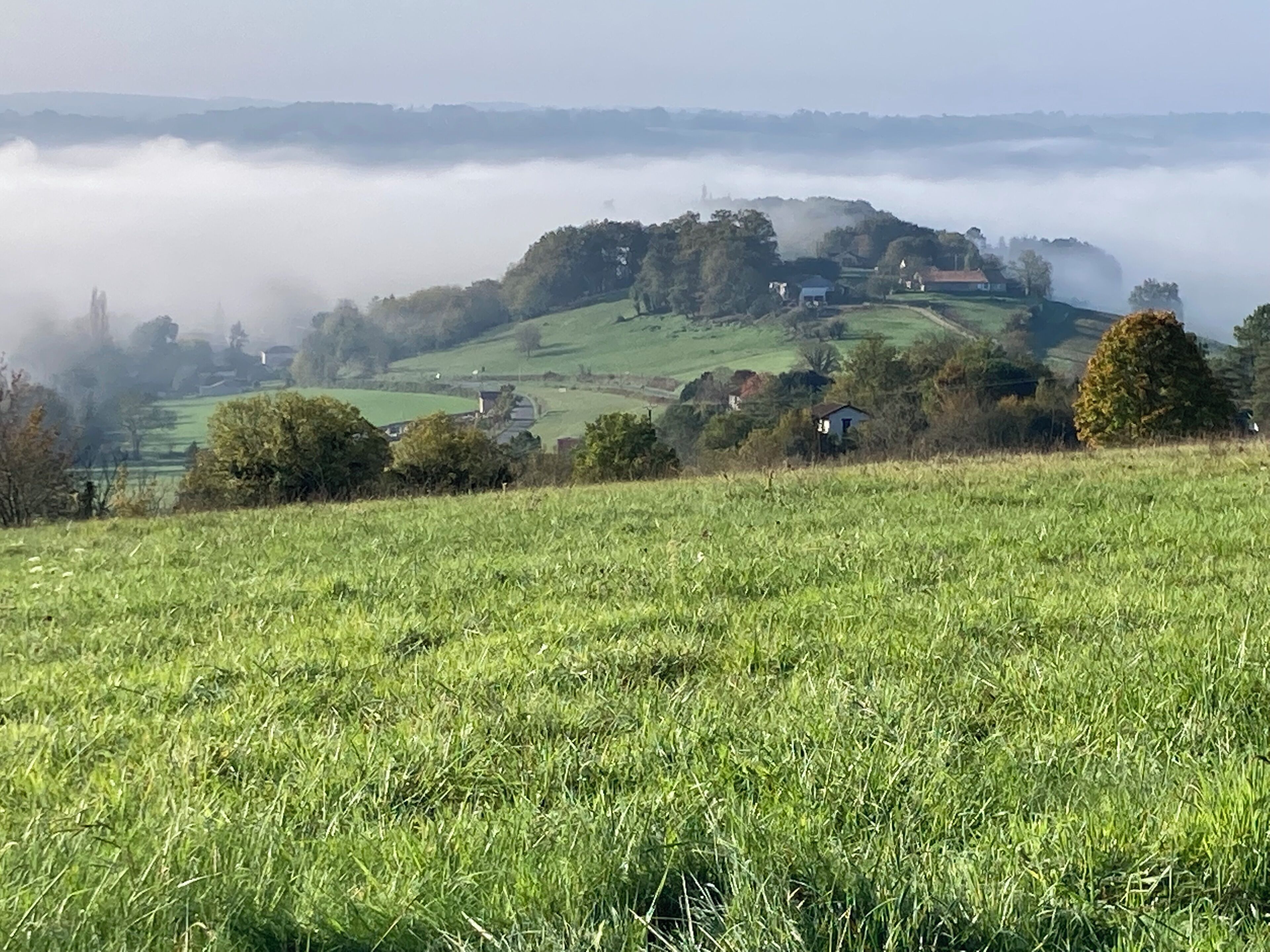 A rural landscape with rolling hills, a mist-covered valley, and scattered houses.