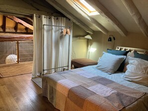 Quarto com cama, mesa de cabeceira, abajur, janela com cortinas e vista para o exterior.