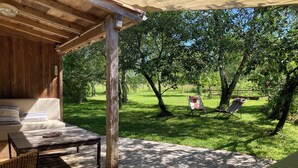 A wooden deck with a sofa and a table, surrounded by a grassy area with trees and a hammock. - Atypical gite in Dordogne-Périgord, quiet, with swimming pool and beautiful view (Manzac-sur-Vern)