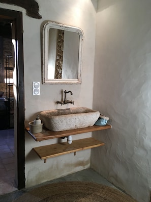 Un baño con lavamanos de piedra, un espejo y una repisa de madera.