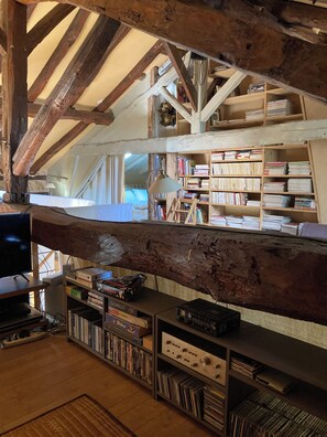 Une pièce avec des poutres apparentes, une bibliothèque remplie de livres, un bureau avec un ordinateur et un téléviseur.
