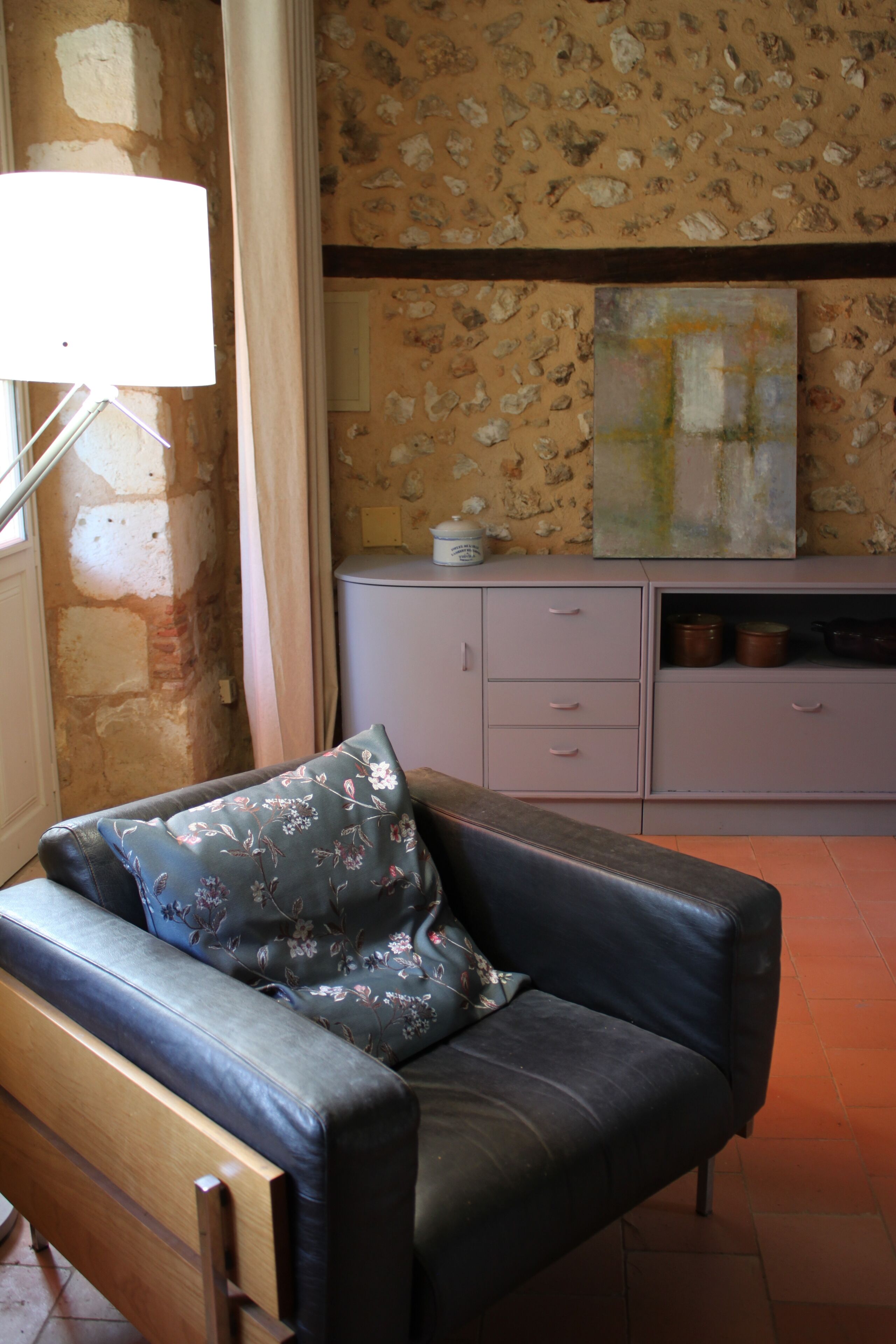 A room with a sofa, a lamp, a cabinet with pots, and a wall with a floral pattern.