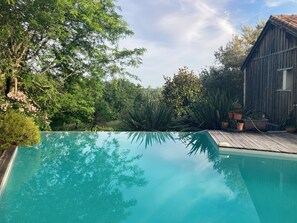 Piscina com deck de madeira, rodeada por vegetação exuberante e um edifício de madeira rústico.