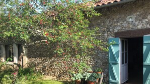 A stone building with a wooden deck, a tree with red berries, and a potted plant. - Atypical gite in Dordogne-Périgord, quiet, with swimming pool and beautiful view (Manzac-sur-Vern)