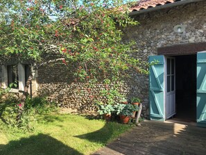 Un edificio de piedra con una terraza de madera, un árbol con bayas rojas y una planta en maceta.