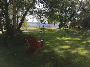 A red Adirondack chair in a grassy area with trees and a distant view of hills. - Atypical gite in Dordogne-Périgord, quiet, with swimming pool and beautiful view (Manzac-sur-Vern)