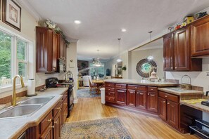 A spacious kitchen with wooden cabinets, a large island, and a view to the dining area. - Cozy house w/ mountain views, deck, outdoor dining, dog-friendly, jacuzzi, w/d (Sylva)
