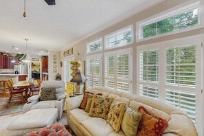 A spacious living room with a large beige sofa, a dining area with wooden chairs, and a kitchen in the background. - Cozy house w/ mountain views, deck, outdoor dining, dog-friendly, jacuzzi, w/d (Sylva)