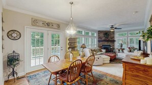 A dining area with a wooden table and chairs, a chandelier, and a fireplace in the background. - Ward Retreat (Sylva)